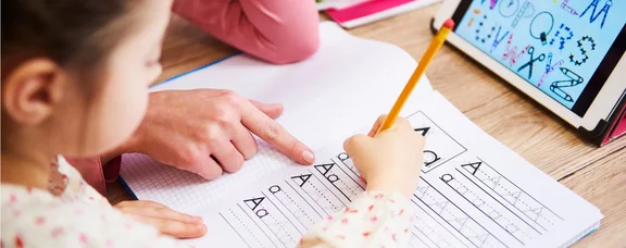 Ein Kind übt, Buchstaben in ein Heft zu schreiben.