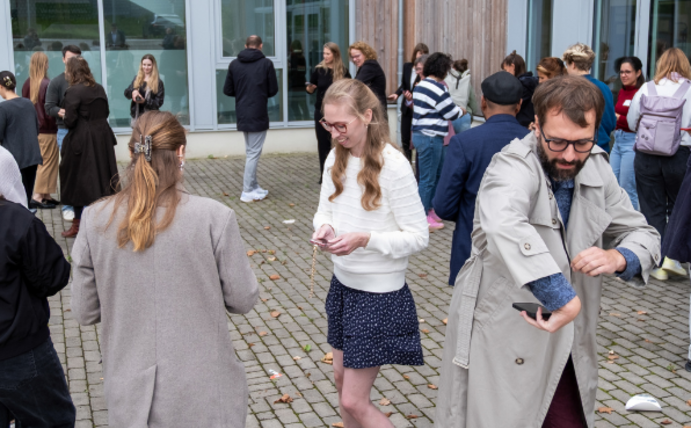 Several people walk across a square and look at their smartphones.