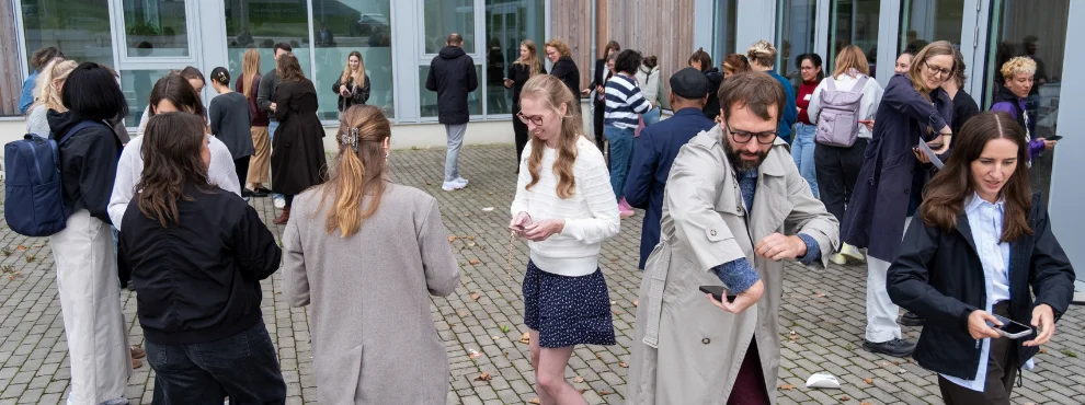 Several people walk across a square and look at their smartphones.
