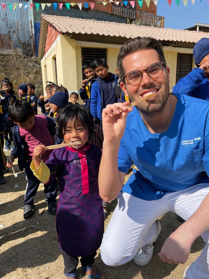 Ein Student der Zahnmedizin posiert, im Rahmen eines Projektes in Nepal, mit einem Kind. Beide halten eine Zahnbürste in der Hand.