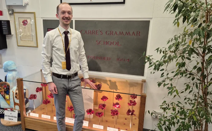 Philipp Raschke is standing in front of a glass display case, above which hangs a school nameplate.