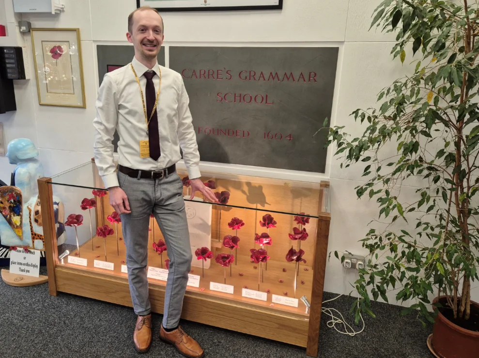 Philipp Raschke is standing in front of a glass display case, above which hangs a school nameplate.