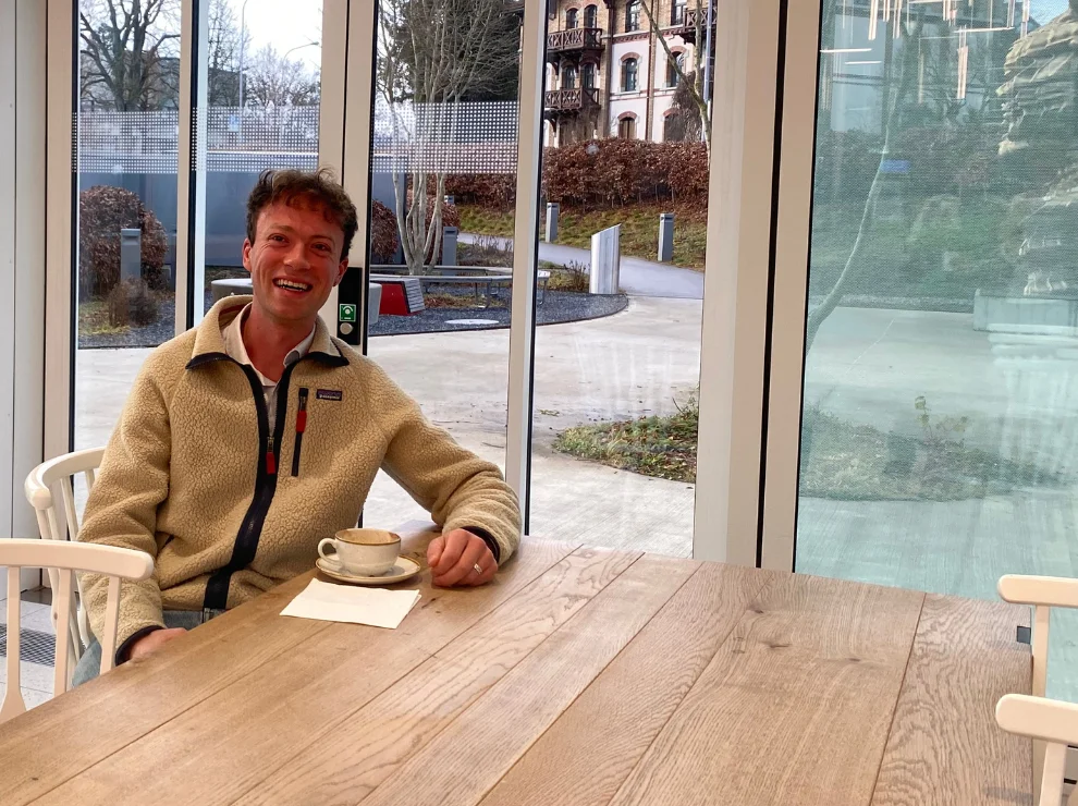 Victor Wolff sitzt mit einer Tasse Kaffee an einem Holztisch.