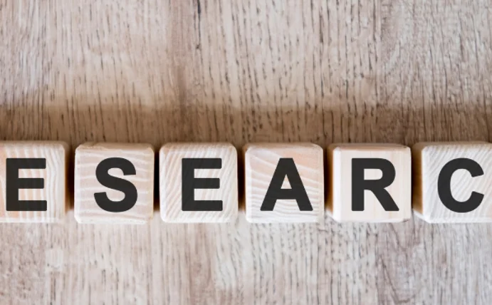 You can see letters on a wooden background spelling out the word “Research” 
