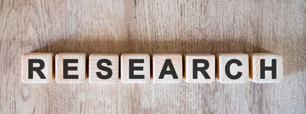 You can see letters on a wooden background spelling out the word “Research” 