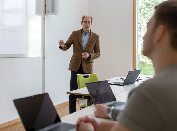 Eine Habilitation an der UW/H ist der erste Schritt zur Professur. (Foto: UW/H | Michael Schwettmann) Ein Professor steht an einer Tafel und erklärte Studierenden etwas.