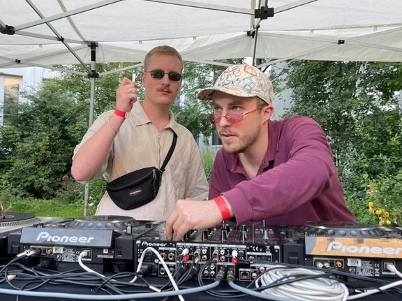 Julian Seitlinger steht zusammen mit einem anderen jungen Mann an einem DJ-Pult.