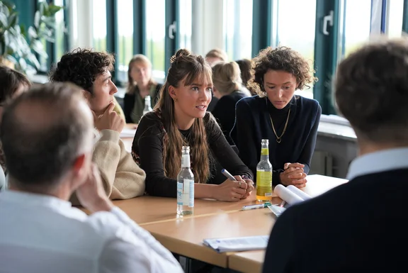 Students sit around a table and discuss.