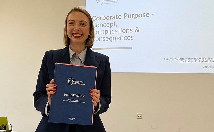 Das RMI Team gratuliert Nicole Steller zu Ihrer erfolgreichen Dispuation (©RMI) Nicole Steller hält ihre Dissertation in der Hand, die sie gerade erfolgreich verteidigt hat (Foto vom RMI)