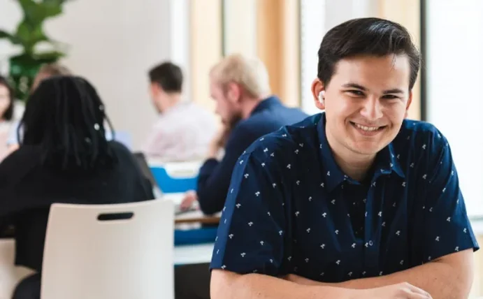 Ein Student sitzt an einem Tisch und lächelt in die Kamera.
