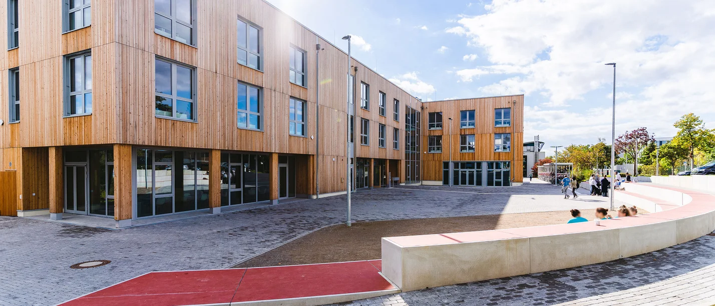 Der Holzbau der Uni Witten/Herdecke: Fast komplett aus nachwachsenden Rohstoffen gebaut (Foto: UW/H | Johannes Buldmann) Bild eines Holzgebäudes mit Vorplatz in der Sonne