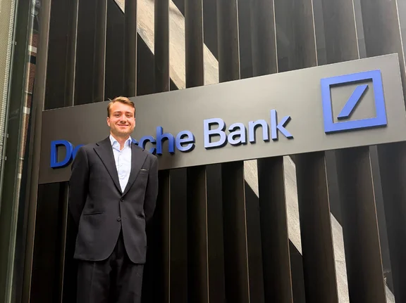 Niklas Kaminski steht vor dem Gebäudeschriftzug der Deutschen Bank.