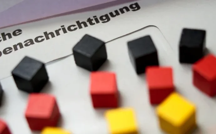 Die amtliche Bescheinigung zur Bundestagswahl liegt flach auf einem Tisch, darauf kleine Holzklötze in der Farbe der Deutschlandflagge.