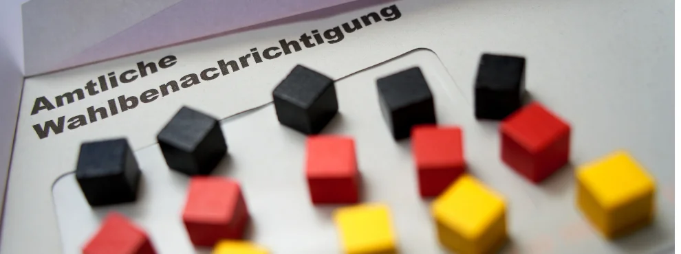Die amtliche Bescheinigung zur Bundestagswahl liegt flach auf einem Tisch, darauf kleine Holzklötze in der Farbe der Deutschlandflagge.