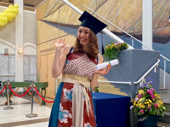 Nicole Steller ist festlich gekleidet, trägt einen Absolvent:innen-Hut und hält ein Diplom in der Hand.