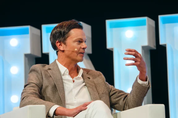 Foto eines Mannes, der in einem hellen Sessel sitzt und gestikulierend spricht.