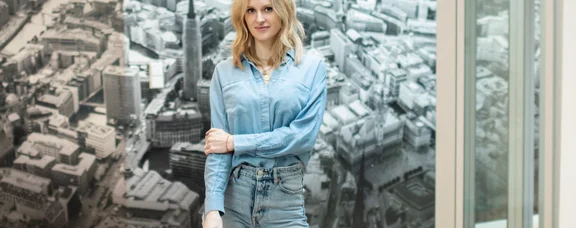 Portrait einer Frau vor einer Fototapete mit dem Motiv einer Großstadt.