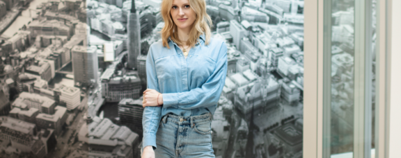 Nach ihrem Studium an der UW/H gründete Lara Daniel die Marketing-Agentur Pulse Advertising. (Foto: Pulse Advertising) Portrait einer Frau vor einer Fototapete mit dem Motiv einer Großstadt.