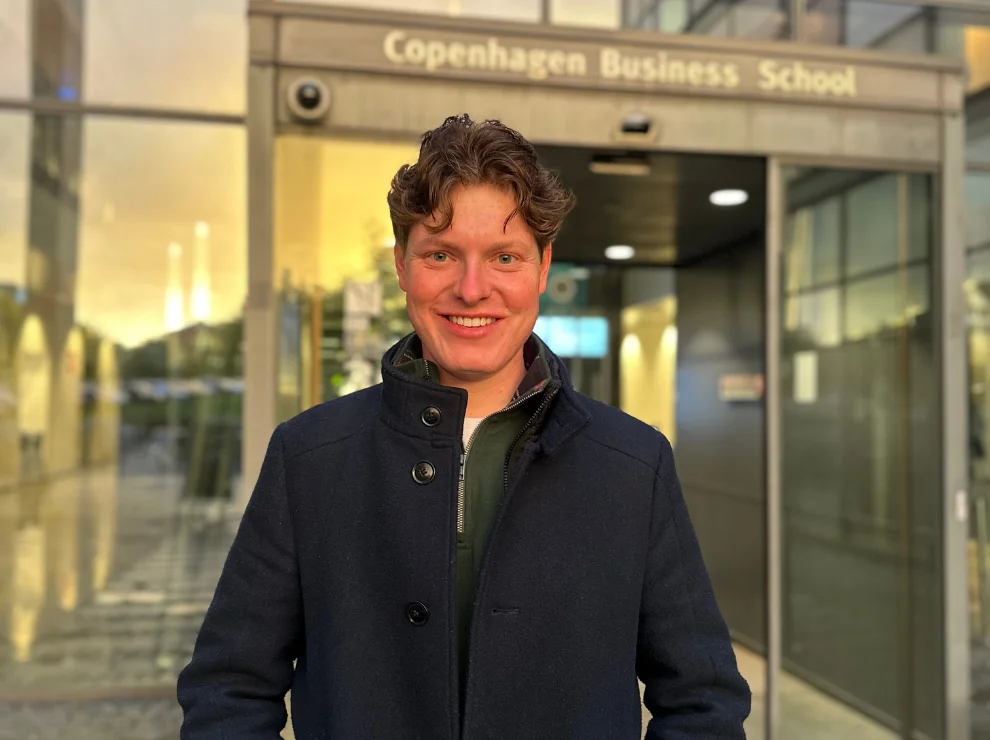 Porträtbild von Moritz Krauss vor einem Gebäude mit Glastüren.