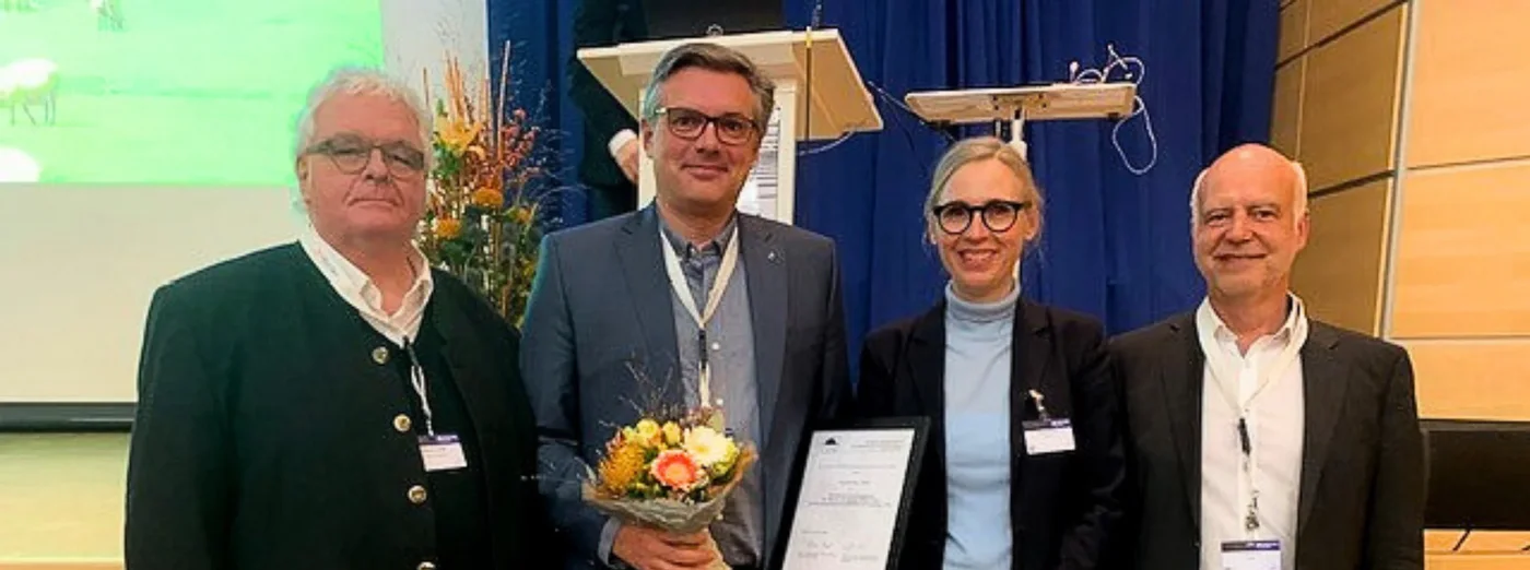 Vier Herren in einer Reihe; einer hält eine Urkunde in der Hand.