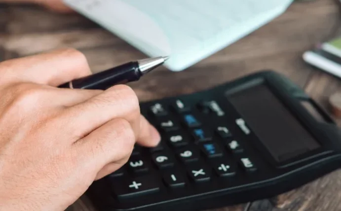 Man sieht eine Hand, die Zahlen in einen Taschenrechner eintippt.