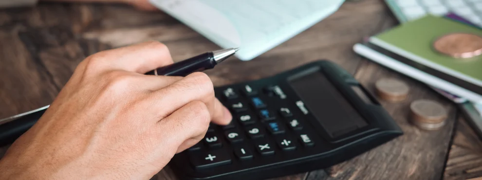 Man sieht eine Hand, die Zahlen in einen Taschenrechner eintippt.