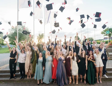 Willkommen im Kreis der erfolgreichen Absolvent:innen an der UW/H (Foto: UW/H I Grubenglück GmbH) Eine Gruppe von Absolvent:innen in festlicher Kleidung wirft Absolvent:innen-Kappen in die Luft.