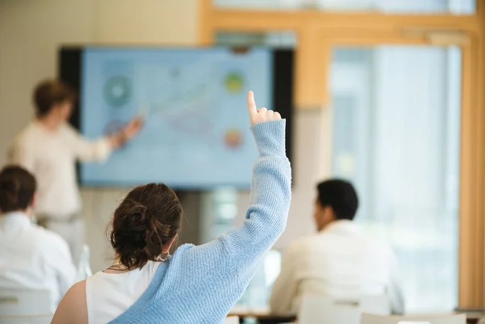 Ein Studentin hebt im Seminar die Hand, um einen Beitrag abzugeben.