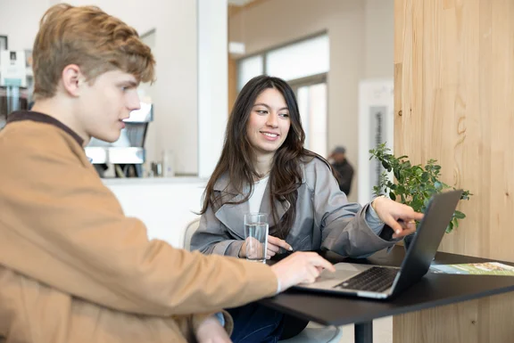 Zwei Studierende schauen zusammen auf einen Laptop.