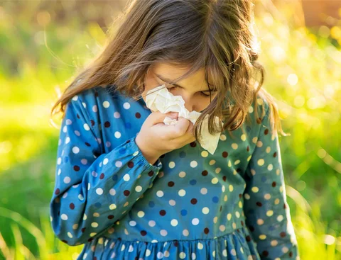 A girl sneezes and holds a handkerchief to her nose.