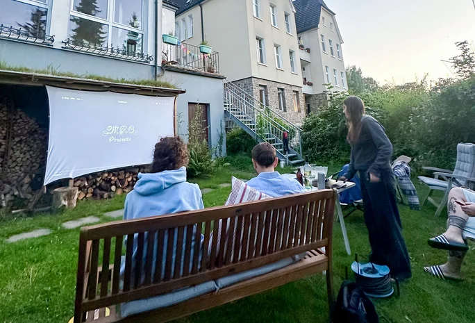 This is life in Witten (Photo: Private) Two students are sitting on a garden bench. They are looking at a screen stretched on the wall of a house.