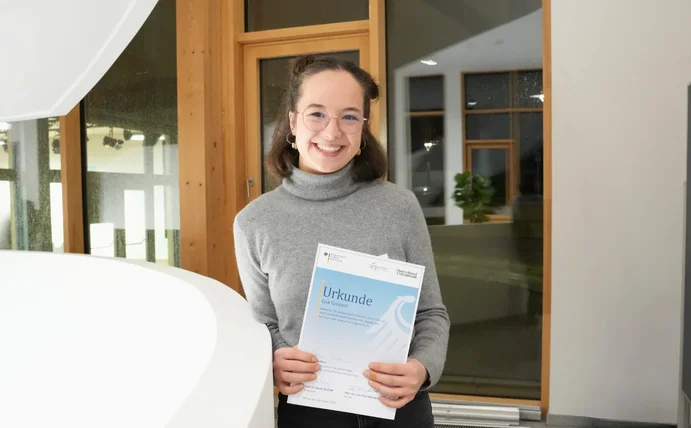 Lisa Kaupert hält ihr Zertifikat vom Deutschlandstipendium und lächelt in die Kamera.
