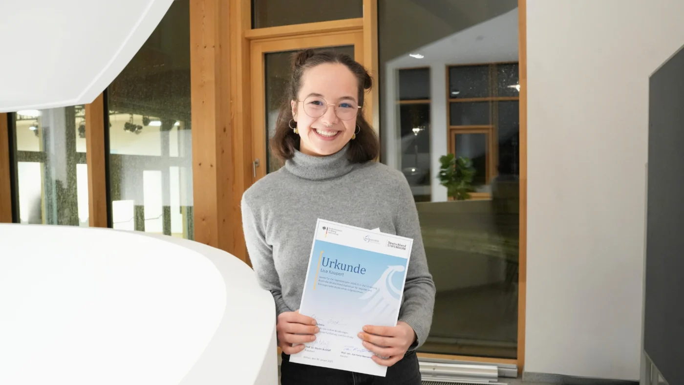 Lisa Kaupert hält ihr Zertifikat vom Deutschlandstipendium und lächelt in die Kamera.