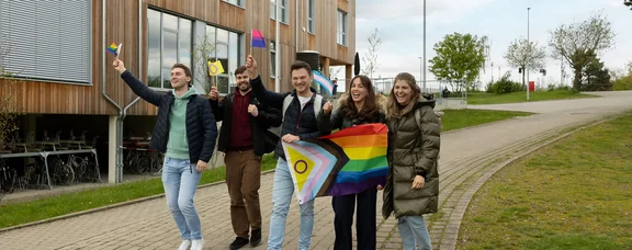 Studierende laufen mit geschwenkten Pride-Flaggen über den Campus.