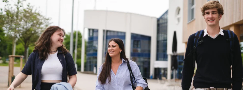 Three students are walking across the campus of Witten/Herdecke University, beaming with joy.