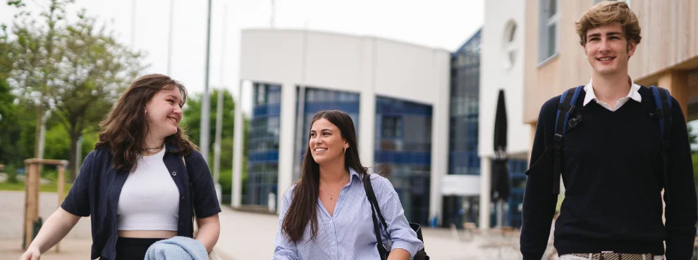 Drei Studierende laufen freudestrahlend über den Campus der Uni Witten/Herdecke.