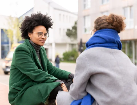 Auf dem Campus der UW/H (Foto: UW/H | Michael Schwettmann) Zwei Studentinnen sitzen auf dem Campus der UW/H und sprechen miteinander.
