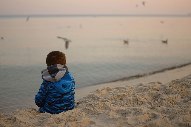Kind sitzt allein im Sand am Meer.