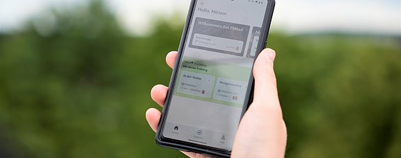 Achtsamkeit to go – mit der 7Mind-App (Foto: UW/H) Eine Person hält ein Smartphone in der Hand. Der Bildschirm zeigt die Startseite einer Meditations-App.