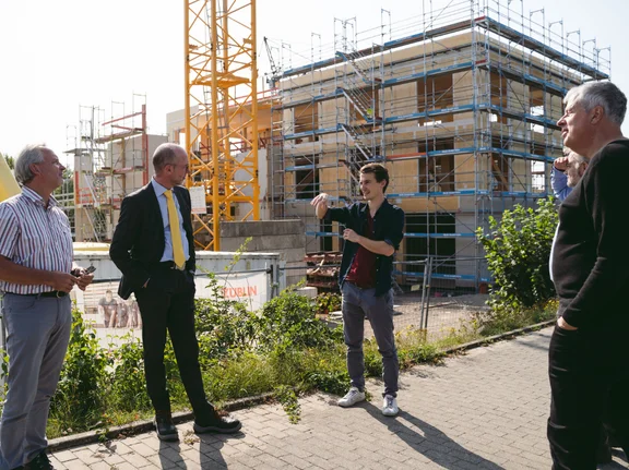 Dominik Treß vor der Baustelle des Holzgebäudes (Foto: UW/H | Johannes Buldmann) Dominik Treß spricht mit anderen Personen vor der Baustelle des Holzgebäudes