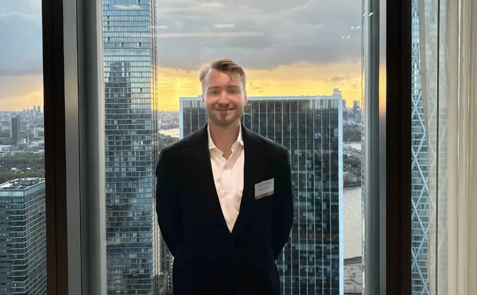 Niklas Kaminski steht vor einer Fensterfront mit Hochhäusern im Hintergrund.