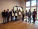 Gruppenfoto, drei Menschen in der Mitte halten eine Urkunde in die Kamera.