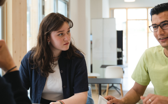 At UW/H, students discuss how they can help shape the economy and society responsibly. (Photo: UW/H I Johannes Buldmann) Three students in conversation in the new building