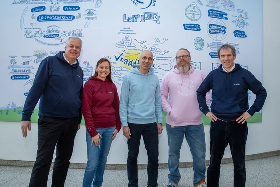 Das Präsidium der UW/H steht in der Haupthalle vor dem Leitbild-Plakat.