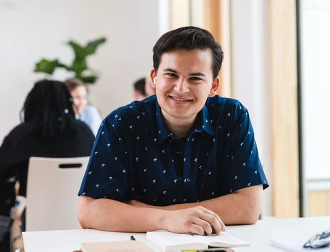 Bewirb dich für den Studiengang Management & Pschologie (B. Sc.) an der UW/H. (Foto: UW/H | Johannes Buldmann) Ein junger Mann sitzt an einem Tisch und hat ein Heft vor sich liegen.