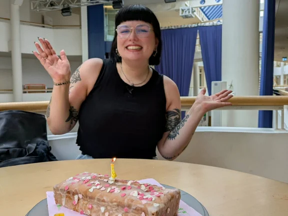 At UW/H, Viktoria has found the space and the community to tackle the issues that matter to her. (Photo: Private) Viktoria Schutschmann is sitting at a table and smiling at the camera. On the table in front of her is a festive cake with a candle on it.