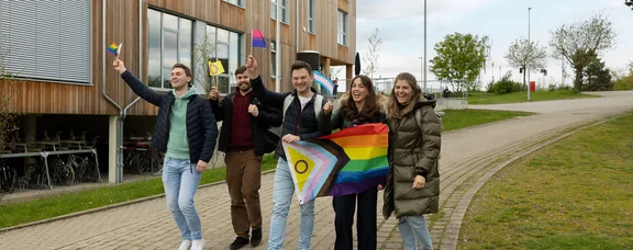Gelebte Vielfalt (Foto: UW/H | Michael Schwettmann) Studierende laufen mit geschwenkten Pride-Flaggen über den Campus.