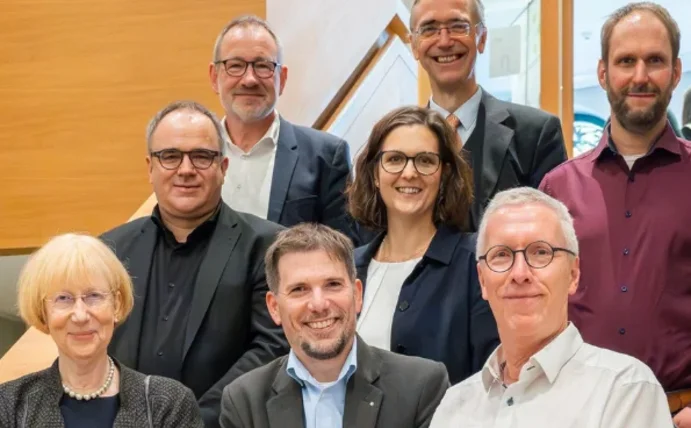 Acht Personen stehen auf einer Treppe und lächeln in die Kamera.