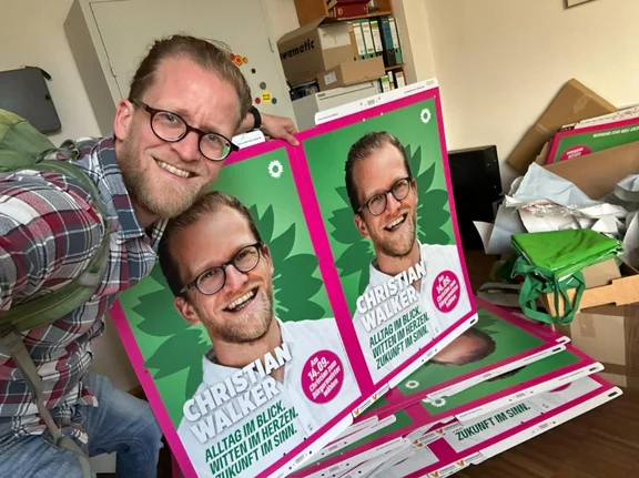 Bei der Kommunalwahl im September 2025 tritt Christian für Bündnis 90/Die Grünen an. (Foto: privat) Ein Mann posiert für ein Foto zusammen mit zwei Wahlplakaten von ihm.