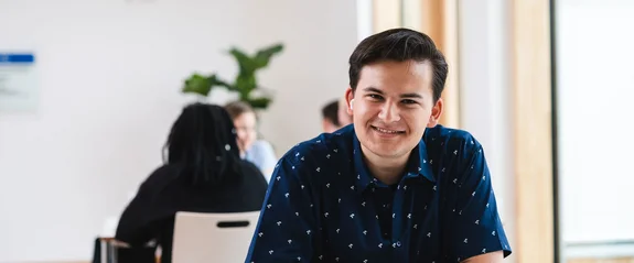 Ein Management & Psychologie (B. Sc.) Student sitzt im Lernflur und schaut direkt in die Kamera.